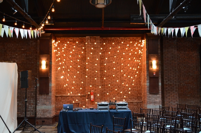 String Lights with multiple swoops against wall with pennant flags suspended at 26 Bridge located in Brooklyn, New York