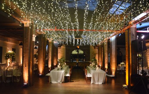 Uplights placed at the base of each column and along perimeter walls with icicle fairy lights suspended above dance floor on 1st floor at The Liberty Warehouse located in Brooklyn, NY