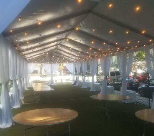 String Lights under an 80ft x 20ft tent hanging in parallel lines with approximately 5ft of space between each parallel line for an outdoor wedding at The Grace Church in NYC. Decorative white sheer curtains hanging at each of the tent's supporting poles.