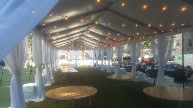 String Lights under an 80ft x 20ft tent hanging in parallel lines with approximately 5ft of space between each parallel line. Decorative white sheer curtains hanging at each of the tent's supporting poles.