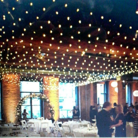 A canopy of String lighting hanging betweeen the center columns along with up-lights along the perimeter walls at The Dumob Loft