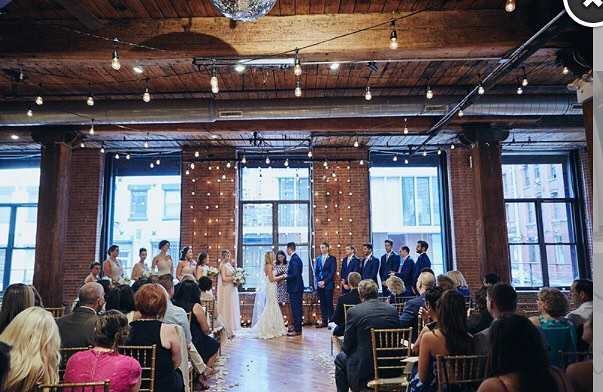 String lighting hanging betweeen the center columns along with string lights hanging vertically behind ceremony at The Dumob Loft