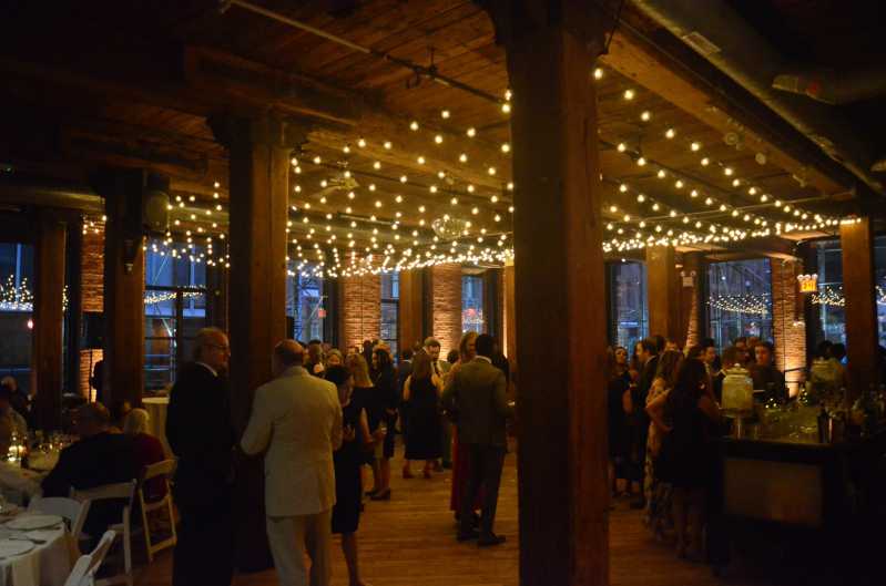 A canopy of String lighting hanging betweeen the center columns along with up-lights along the perimeter walls at The Dumob Loft