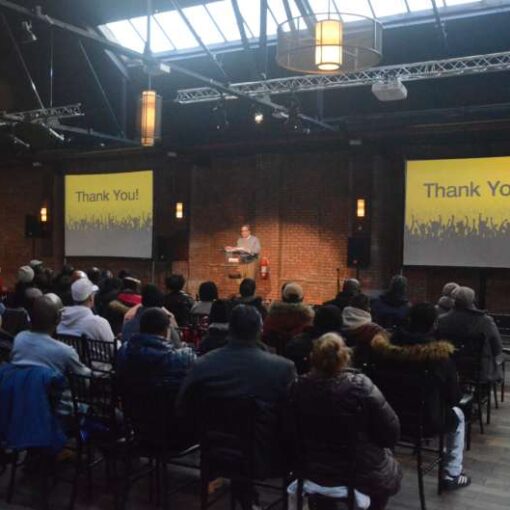 A Projector suspended overhead from a Truss with a screen mounted on the wall and a spotlight with additional AV equipment was provided for a corporate event hosted at 26 Bridge in Brooklyn, NY.