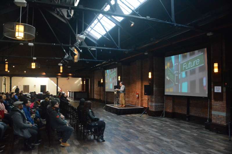 A Projector suspended overhead from a Truss with a screen mounted on the wall with a spotlight, stage, and additional AV equipment was provided for a corporate event hosted at 26 Bridge in Brooklyn, NY.