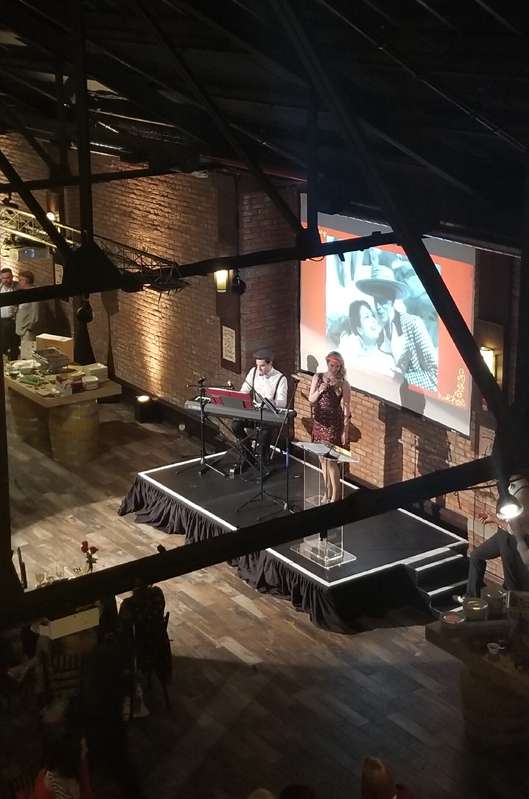 A Projector suspended overhead from a Truss with a screen mounted on the wall and a spotlight with additional AV equipment and stage was provided for the Louie Awards hosted at 26 Bridge in Brooklyn, NY.