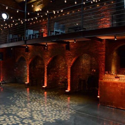 String Lights (Cafe / Bistro) with Warm White bulbs suspended vertically and overhead in the main room for a wedding at The Foundry with Up-lights along the perimeter walls and a stock gobo projected on the floor.