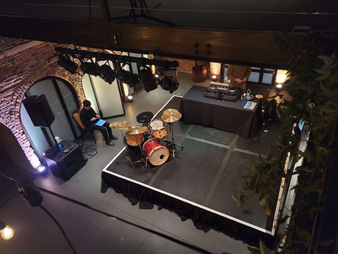 A 12ft x 12ft stage in the main room under the mezzanine level near the entrance doors with dimmable spotlights suspended overhead at The Foundry.