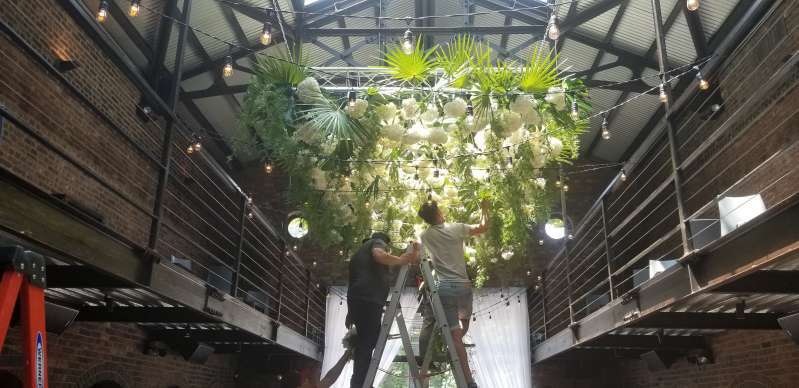 Florals attached to a rectangular truss hanging overhead in the main room for a wedding at The Foundry.