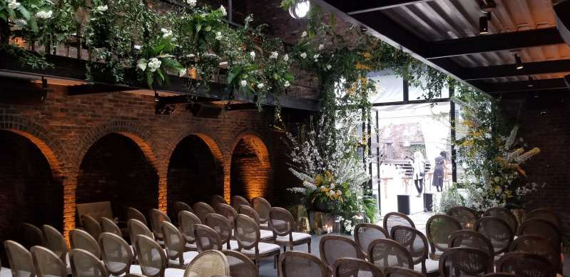 Up-Lights placed along the perimeter walls of the main room at the foundry, with florals along the mezzanine railing.