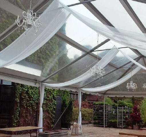 White sheer drapes hanging in parallel lines with Chrystal Chandeliers under a clear-top tent in the rear courtyard at The Foundry.