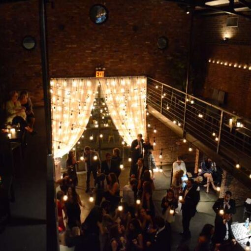Warm White String Lights are hanging overhead above the main floor and vertically at the rear courtyard doors for a wedding at The Foundry.