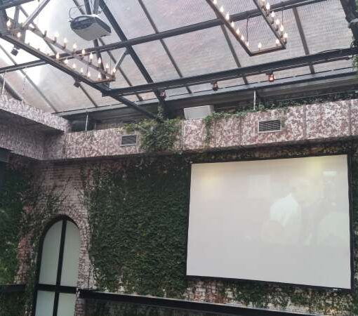 A projector and Screen are hanging in the greenhouse at The Foundry for a video presentation during a wedding.