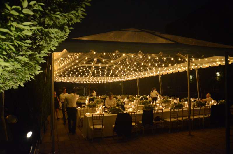 String lighting with warm white bulbs hangs in parallel lines under a tent in the courtyard at The Foundry for a wedding.