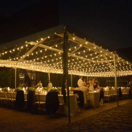 String lighting with warm white bulbs hangs in parallel lines under a tent in the courtyard at The Foundry for a wedding.