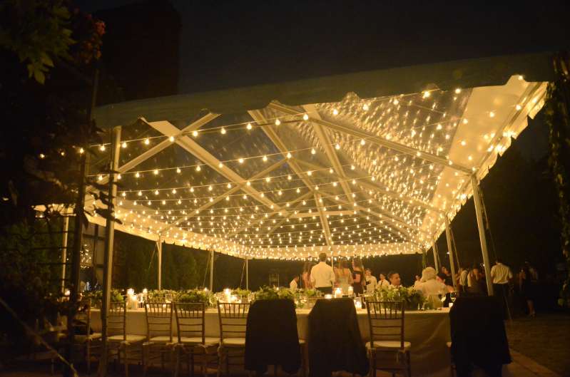String lighting with warm white bulbs hangs in parallel lines under a tent in the courtyard at The Foundry for a wedding.