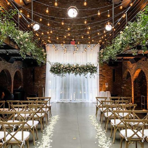String Lights with warm white bulbs and florals hanging overhead with Up-Lights along the perimeter walls.