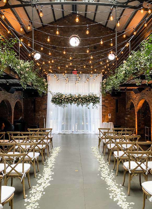 String Lights with warm white bulbs and florals hanging overhead with Up-Lights along the perimeter walls.