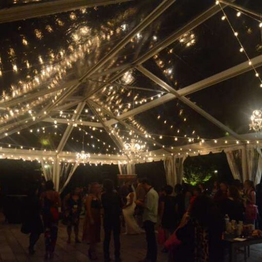 Crystal Chandeliers aand String lighting with warm white bulbs hangs in random zigzagging lines under a tent in the courtyard at The Foundry for a wedding.