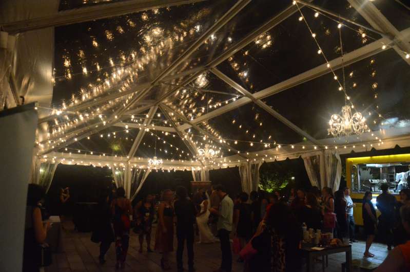 Crystal Chandeliers aand String lighting with warm white bulbs hangs in random zigzagging lines under a tent in the courtyard at The Foundry for a wedding.