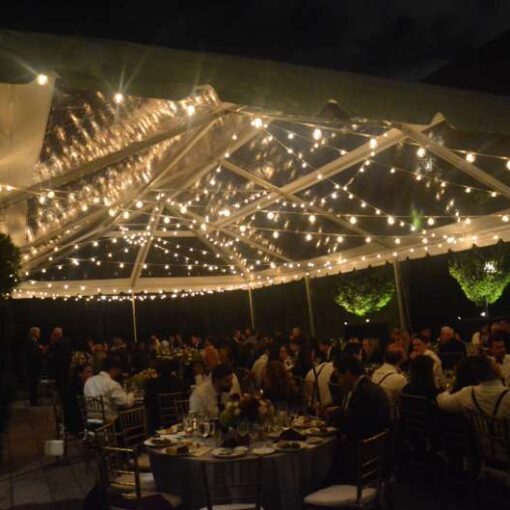 String lighting with warm white bulbs hangs in random zigzagging lines under a tent in the courtyard at The Foundry for a wedding.