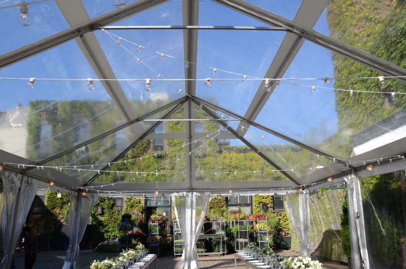 String lights are hanging under a clear-top tent for a wedding in the rear courtyard at The Foundry.
