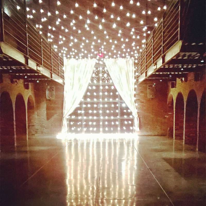 A canopy of warm white string lights hanging across the mezzanine level and String Lights hanging vertically against the rear courtyard doors for a wedding at The Foundry.