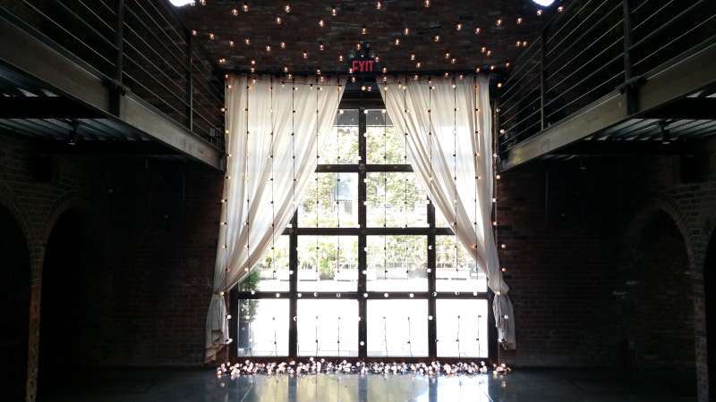 A canopy of warm white string lights hanging across the mezzanine level and String Lights hanging vertically against the rear courtyard doors for a wedding at The Foundry.