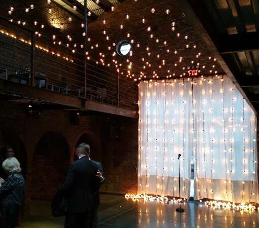 A canopy of warm white string lights hanging across the mezzanine level and String Lights hanging vertically against the rear courtyard doors for a wedding at The Foundry.