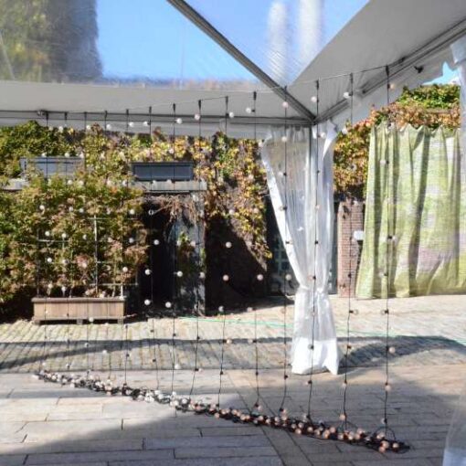 String lights are hanging vertically in the corner of the tent for a wedding in the courtyard at The Foundry.