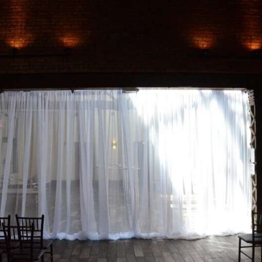 White Sheer Curtains hanging as a backdrop behind ceremony area for a wedding at 26 Bridge.