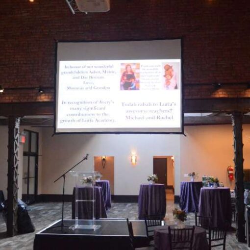String Lights WITH Pendants Lamps hanging in the main room with a projector and screen and Up-Lights, stage, podium at 26 Bridge