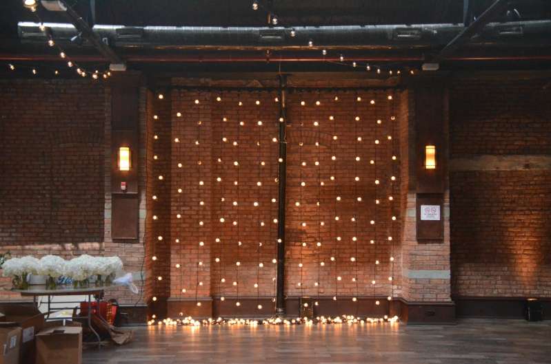 String Lights hanging vertically as a backdrop of lights with Warm White Up-Lights against the perimeter walls of 26 Bridge.