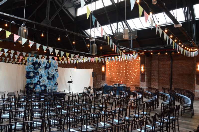 String Lights along with Bunting Flags hanging over the majority of the main room for a wedding at 26 Bridge. A backdrop of String light hanging with multiple horizontal swoops behind against a wall at 26 Bridge.