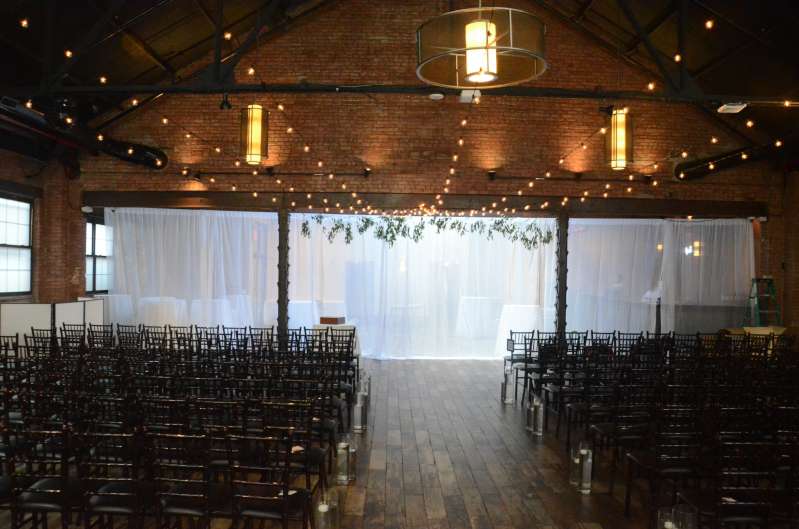 String Lights with round G50 Bulbs are hanging in a V-shaped pattern between the 3rd and 5th Beams in the Main Room for a wedding at 26 Bridge.