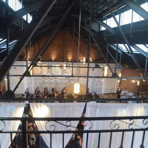 String lights are hanging between the 2nd and 3rd beams in the main room for a wedding at 26 Bridge.