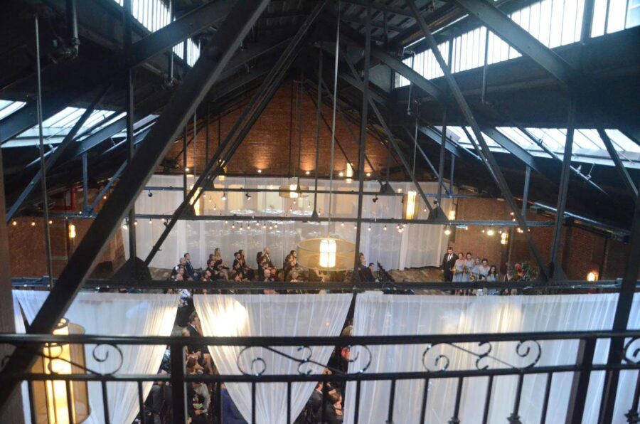 String lights are hanging between the 2nd and 3rd beams in the main room for a wedding at 26 Bridge.