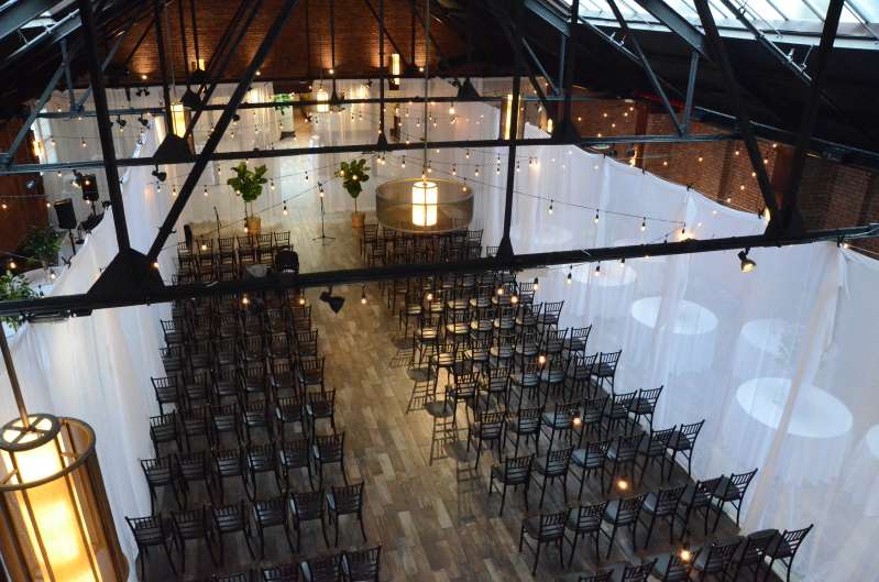 String Lights hanging in a zigzag pattern between Entrance Wall and 4th beam for a wedding in the main room at 26 Bridge.  Also, White Sheer Clip-On Curtains hang the length of the left and right side of the main room from the entrance wall to the 4th beam that crosses the width of the room.  Also, an additional set of white sheer Clip-On curtains hanging across the with of the main room under the 4th beam.