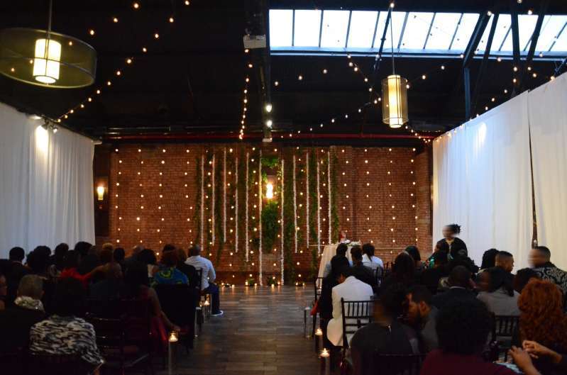 String Lights hanging vertically as a backdrop behind the ceremony at 26 Bridge. Along with String Lights hanging in two circular/star shape patterns above the main room at 26 Bridge.