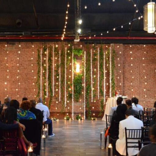 String Lights hanging vertically as a backdrop behind the ceremony at 26 Bridge. Along with String Lights hanging in two circular/star shape patterns above the main room at 26 Bridge.