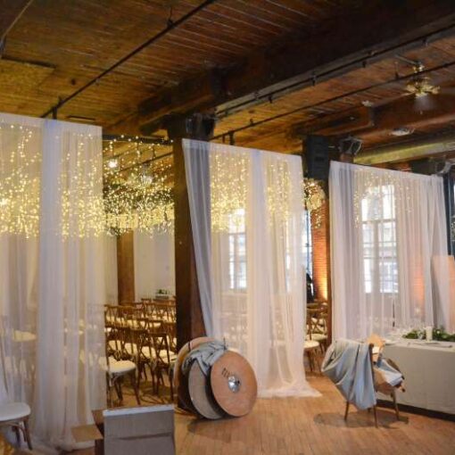 Fairy (Icicle) Lights hanging between the center columns for a wedding at The Dumbo Loft. Also, Up-Lights at the base of each column between windows.