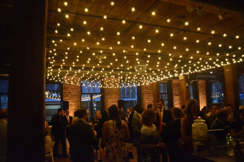 A canopy of string lights with round G50 bulbs hanging between the center columns at The Dumbo Loft. Also, Up-lights are set at the base of each column between the windows.