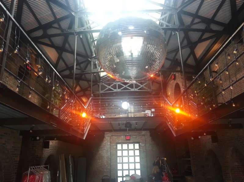 A 40" Disco Ball hanging between the railing of the mezzanine level in the main room at The Foundry. String Lights draped along the railing of the mezzanine level.