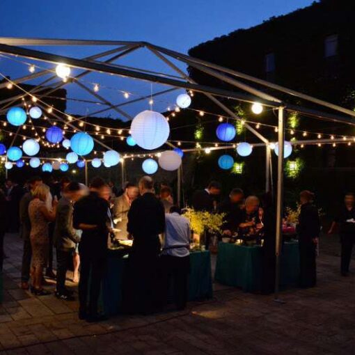 String lights with paper lanterns are hanging under a tent frame for a wedding in the rear courtyard at The Foundry.