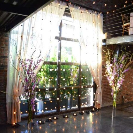 Warm white string lights hanging across the mezzanine level and String Lights hanging vertically against the rear courtyard doors for a wedding at The Foundry.
