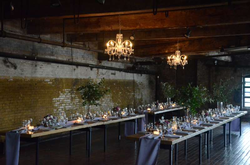 Crystal chandeliers are hanging under the lower ceiling area on the sides of the main floor at The Greenpoint Loft for a wedding.