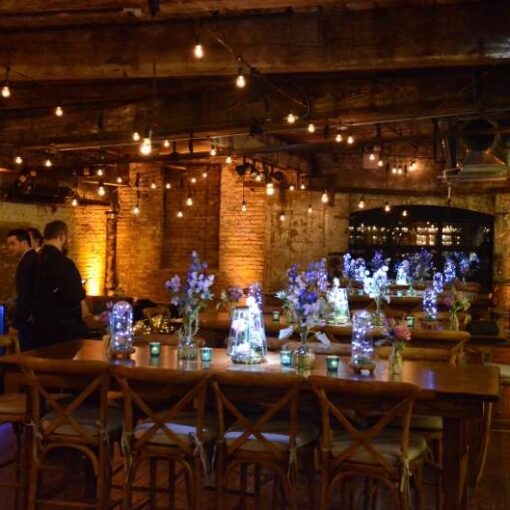 Warm White String Lights are hanging in parallel lines under the lower ceiling area on the main floor for a Bat Mitzvah at The Greenpoint Loft with Up-Lights.