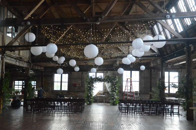 Twinkle Lights with Paper Lanterns hanging between the six center columns for a wedding in the main room at The Greenpoint Loft.