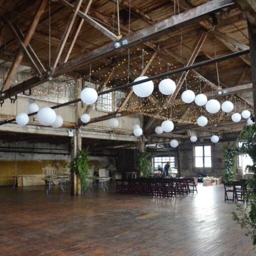 Twinkle Lights with Paper Lanterns hanging between the six center columns for a wedding in the main room at The Greenpoint Loft.