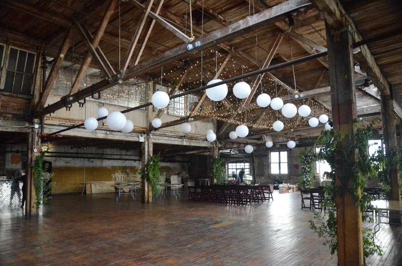 Twinkle Lights with Paper Lanterns hanging between the six center columns for a wedding in the main room at The Greenpoint Loft.